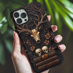 May include: A dark brown phone case with a detailed relief design. The case features a deer skull with antlers, small skulls, and floral accents. The design is carved into the case, giving it a textured appearance.