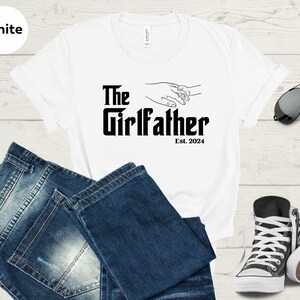 May include: White t-shirt with black text that reads "The Girlfather Est. 2024" and a line drawing of two hands holding each other.