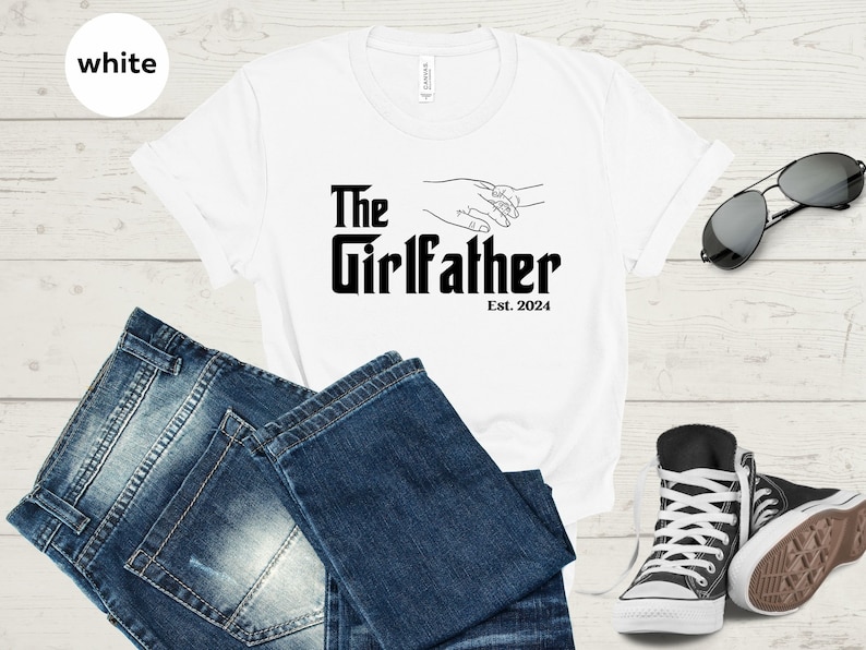 May include: White t-shirt with black text that reads "The Girlfather Est. 2024" and a line drawing of two hands holding each other.