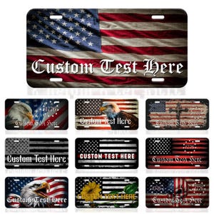 May include: License plate featuring a distressed American flag design with the text "Custom Test Here" in a decorative font. The plate has a rectangular shape with rounded corners and mounting holes.
