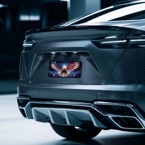 May include: A black car with a license plate featuring an American bald eagle with its wings spread wide, flying over an American flag. The eagle is in front of a blue and white background with stars.