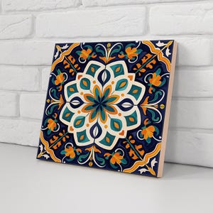 Op de afbeelding: Vierkante keramische tegel met een bloemmotief. De tegel heeft een marineblauwe achtergrond met een centrale bloem in wit, teal en oranje. De rand heeft oranje en gele bloempatronen.