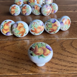 May include: A set of 18 white ceramic cabinet knobs featuring a pear and plum design. The knobs have a glossy finish and are ideal for adding a touch of farmhouse charm to any kitchen or bathroom.
