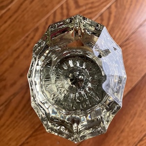 May include: A clear glass door knob with a faceted design. The knob is circular with a raised centre.