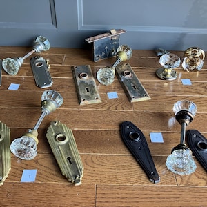 Peut inclure: Assortiment de boutons de porte anciens dans différents styles et finitions, notamment en laiton, en argent et en noir. Certains boutons sont ornés de cristaux de verre transparents.