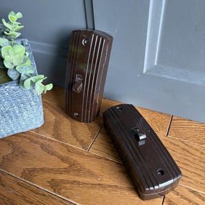 May include: Two dark brown rectangular light switches with a vertical ribbed texture. Each switch features a central toggle lever with the word OFF embossed on it, and two circular screw holes at the top and bottom for mounting purposes.
