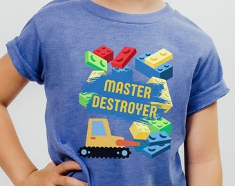 May include: A blue t-shirt with a graphic of a yellow toy bulldozer and colorful toy building blocks. The text "Master Destroyer" is printed on the shirt.