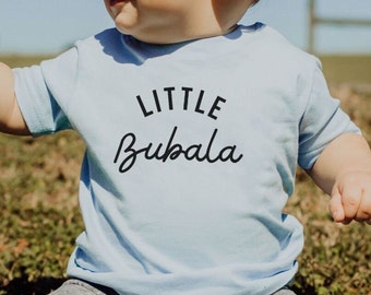 May include: A light blue baby t-shirt with the text "LITTLE BUBALA" printed in black.