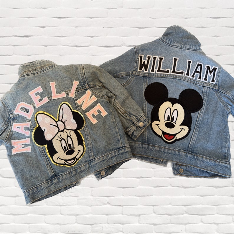 Op de afbeelding: Twee spijkerjacks met gepersonaliseerde patches. Een jack heeft een roze "MADEINE" patch en een Minnie Mouse patch. De andere jack heeft een zwarte "WILLIAM" patch en een Mickey Mouse patch.