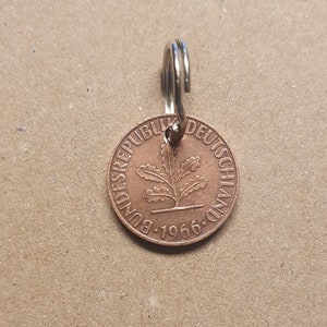 Könnte beinhalten: Eine kupferfarbene Münze mit der Aufschrift "Bundesrepublik Deutschland" und dem Jahr "1966" am Rand. In der Mitte der Münze befindet sich ein stilisiertes Eichenblatt. Die Münze ist an einem silbernen Schlüsselring befestigt.