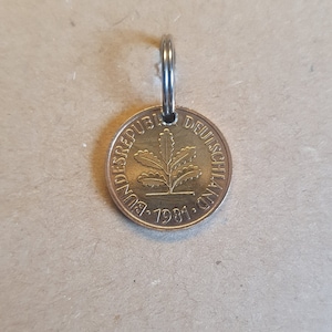 Könnte beinhalten: Ein goldfarbener Münzen-Schlüsselanhänger mit dem Text "Bundesrepublik Deutschland 1981" und einem Eichenblatt-Design.