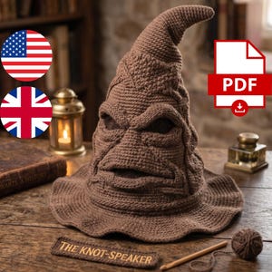 May include: A brown crocheted hat with a pointed, folded top and a wide, wavy brim. The hat features a textured surface with deep folds resembling a face, including prominent brow ridges and a mouth-like opening. A label reads THE KNOT-SPEAKER.