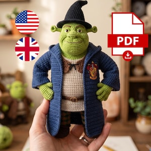May include: A green crocheted ogre doll wearing a black pointed hat, a dark blue hooded robe with a crest on the chest, a beige tunic, and a brown belt. The doll features large ears and a textured yarn finish. A PDF icon is visible in the corner.
