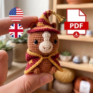 May include: A small brown crocheted animal figure wearing a maroon and gold wizard hat with a gold tassel and a matching maroon and gold cape. The figure has a white muzzle, black eyes, and small ears. The item is presented as a digital PDF pattern.