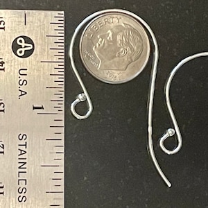 May include: Two silver earring hooks with small round balls at the end. The hooks are shown next to a US dime for size comparison.