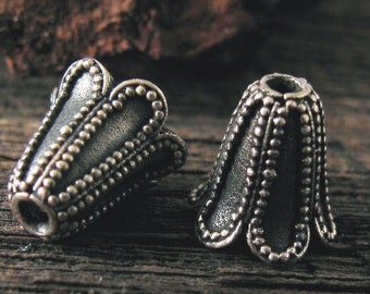 May include: Two silver metal bead caps with a scalloped edge and a textured surface. The caps are designed to be used on the ends of cords or chains.