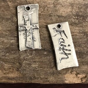 May include: Two silver charms, one with a cross design and the other with the word "Faith" engraved on it.