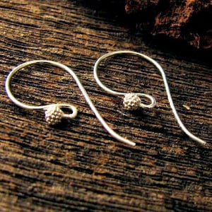 May include: A pair of silver earrings with small, textured ball accents at the ends. The earrings are made of thin, wire-like metal and have a simple, elegant design.
