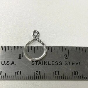 May include: A silver-toned metal charm in the shape of a circle with a beaded edge. The charm is about 1 inch in diameter and is measured against a ruler.