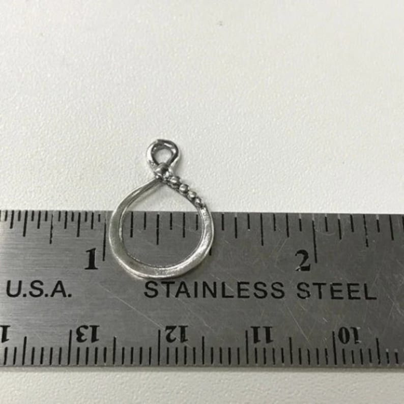 May include: A silver-toned metal charm in the shape of a circle with a beaded edge. The charm is about 1 inch in diameter and is measured against a ruler.