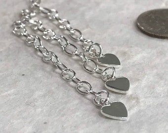 May include: Three silver chains with heart-shaped charms hanging from the ends. The chains are linked together and are silver in color.