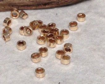 May include: A group of gold-coloured metal jump rings, scattered on a white surface. The jump rings are small and round, with a hole in the centre.