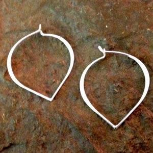 May include: A pair of silver hoop earrings with a teardrop shape. The earrings are simple and elegant.