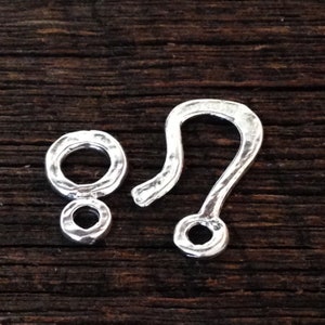 May include: Silver-toned metal clasp with a textured finish. The clasp has two parts: a loop with a smaller loop attached and a hook with a round opening.
