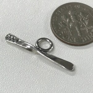 May include: Silver charm in the shape of a ski with a small round bead at the top. The charm has a loop for attaching to a bracelet or necklace.