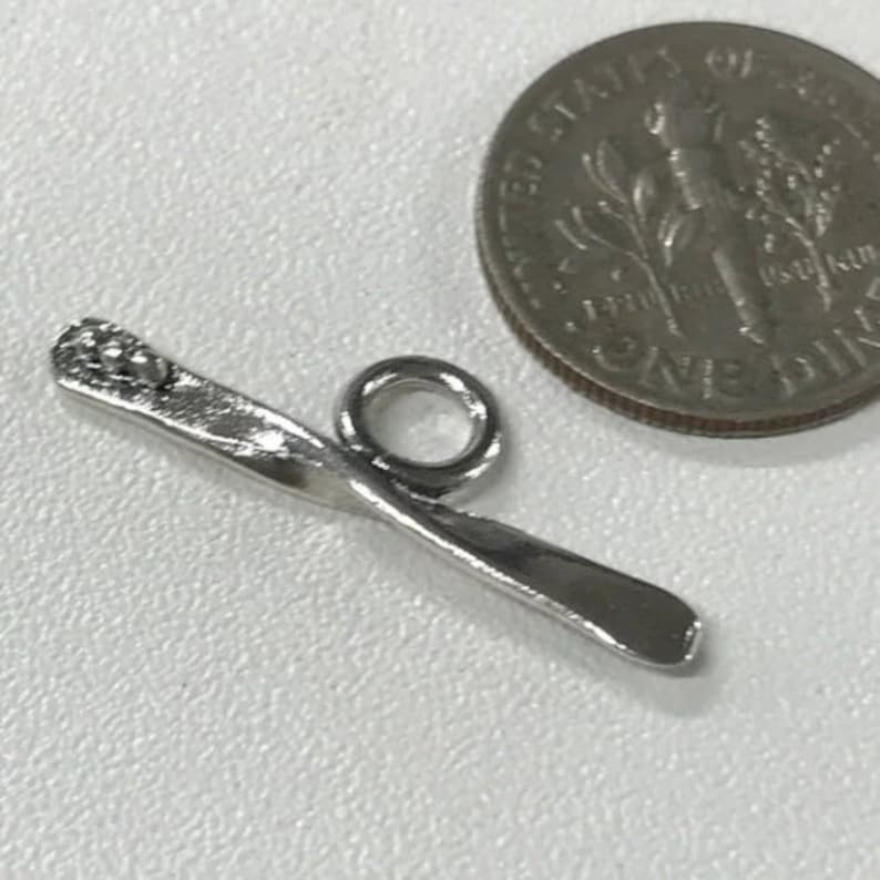 May include: Silver charm in the shape of a ski with a small round bead at the top. The charm has a loop for attaching to a bracelet or necklace.