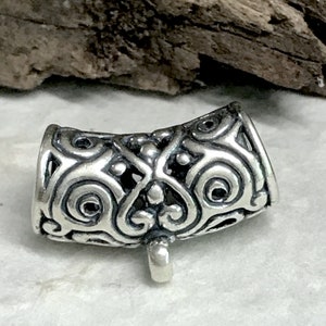 Puede incluir: Cuente de metal plateado con un diseño intrincado y ornamentado. La cuenta tiene un agujero en el centro y un bucle en la parte inferior.