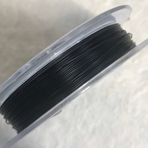 May include: A spool of black thread wound around a clear plastic bobbin.