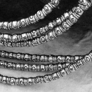 May include: A close-up of a silver necklace with multiple strands of beads. Each bead has a textured, circular design.