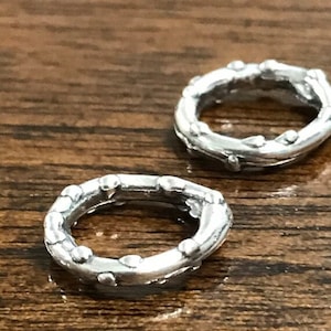 May include: Two silver charm spacers with a textured, twig-like design and small beads around the edges.