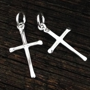 May include: Two silver cross charms, one larger than the other, on a dark wooden background.