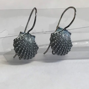 May include: A pair of silver tone earrings with a seashell design. The earrings are made of metal and have a hook closure.