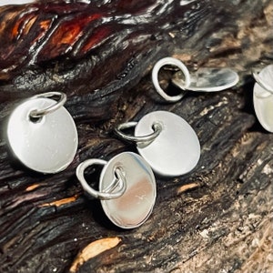 May include: Five silver round charms with jump rings. The charms are smooth and have a shiny finish.