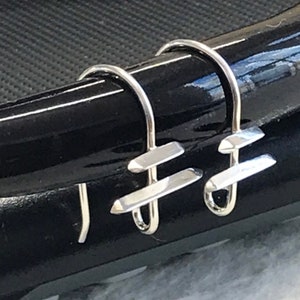 May include: A pair of silver hoop earrings with a geometric design. The earrings are made of a thin wire that is bent into a hoop shape. The wire is then twisted to create a geometric design in the center of the hoop.