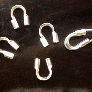 May include: Five silver-toned metal crimp beads, each with a loop on one end and a closed end on the other. The beads are arranged in a semi-circle on a dark surface.