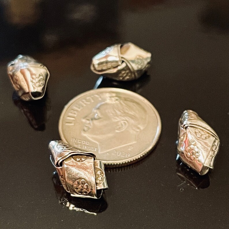 May include: Four silver metal beads with a knot design. The beads are about the size of a US dime.