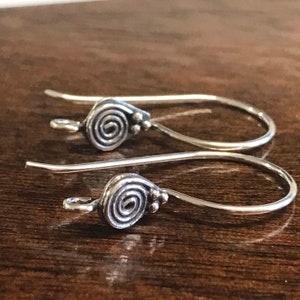 May include: A pair of silver earrings with a spiral design. The earrings are made of a thin wire and have a small loop at the top for attaching to an earring hook.