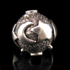 May include: A silver charm in the shape of a sphere with a textured surface and raised geometric designs.