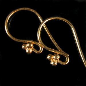 May include: A pair of gold-toned earrings with a simple, elegant design. Each earring features a small, teardrop-shaped loop with three tiny beads at the bottom.