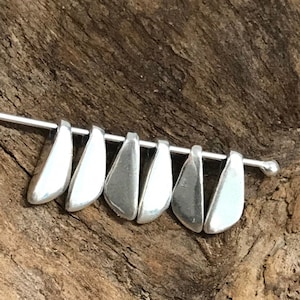 May include: A close-up of seven silver metal pendant bails, arranged in a row on a wooden surface. The bails are teardrop shaped and have a smooth, polished finish.