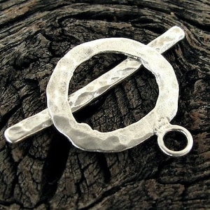 May include: Silver toggle clasp with a hammered finish. The clasp has a round ring with a bar that goes through it.