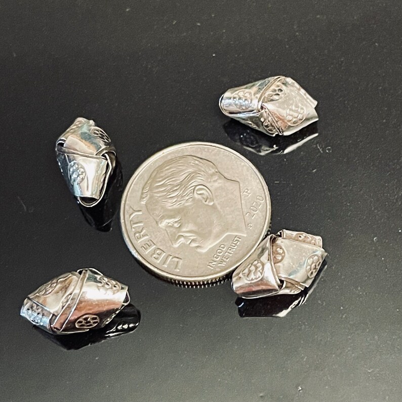 May include: Four silver metal beads with intricate designs, each bead is about the size of a US dime.