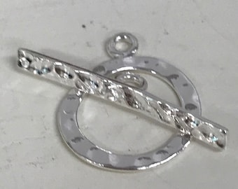 May include: Silver toggle clasp with a textured bar and a hammered circle. The clasp is designed to be used for necklaces, bracelets, or other jewelry.