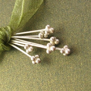 May include: A silver pendant featuring a cluster of small, round, silver beads arranged in a flower-like shape. The pendant is attached to a thin silver chain.