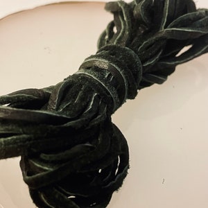 Puede incluir: Un primer plano de un cordón de cuero verde oscuro, retorcido y enrollado. El cordón es suave y flexible, con una superficie ligeramente texturizada.