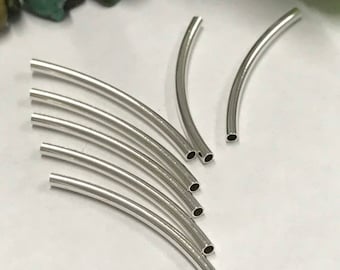May include: Close-up of several curved, silver-colored metal tubes. The tubes have a smooth, shiny surface and are arranged in a fan-like pattern. The ends of the tubes are hollow, revealing a dark interior. The background is a plain white surface.